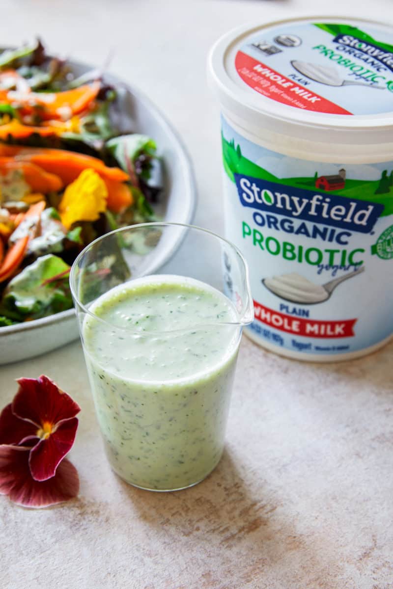 Green goddess dressing in a glass next to Stonyfield organic yogurt and a summer salad.