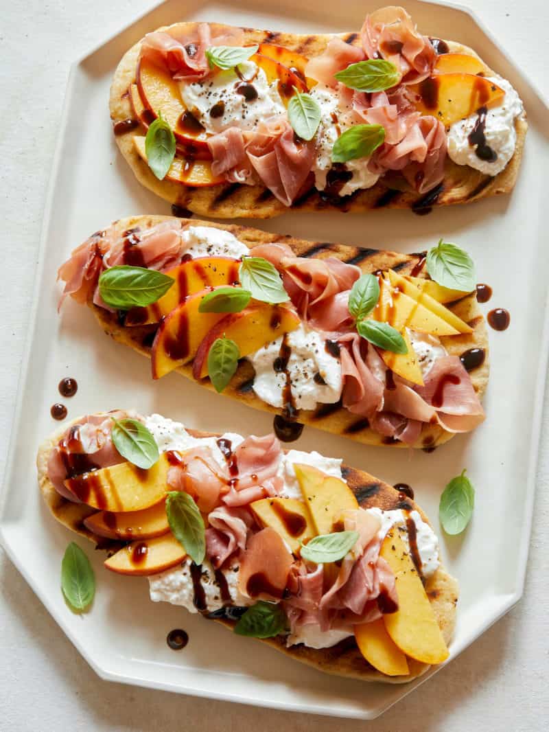 Grilled flatbreads topped with peach, prosciutto, and burrata.