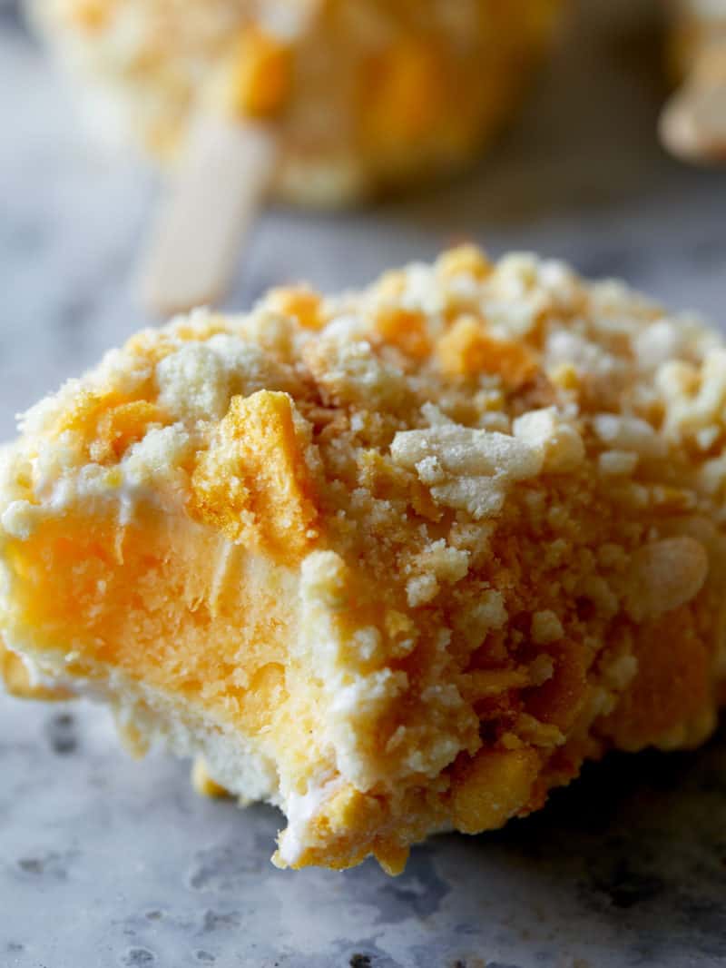 A close up of a half eaten cookie coated mango Lassi frozen yogurt bar.