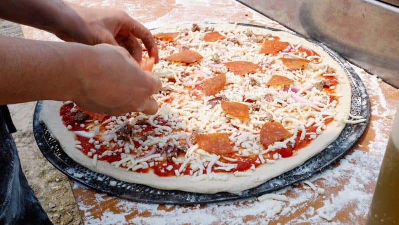 A uncooked pizza being topped with pepperoni triangles.