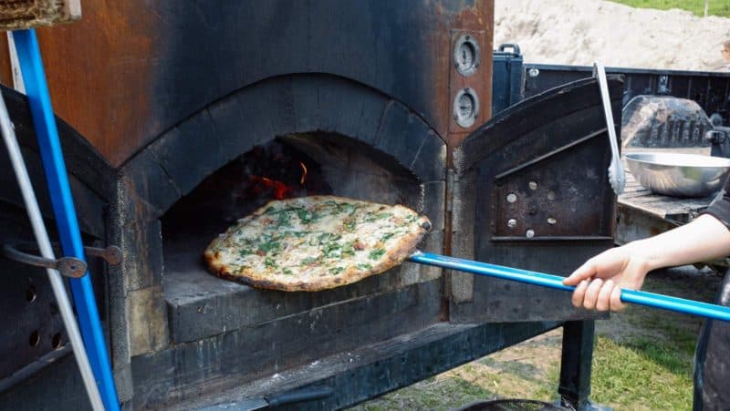 A pizza being removed from a wood burning pizza oven.