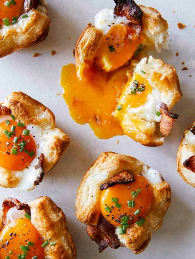 A close up of cheesy flaky breakfast cups with broken yolk.