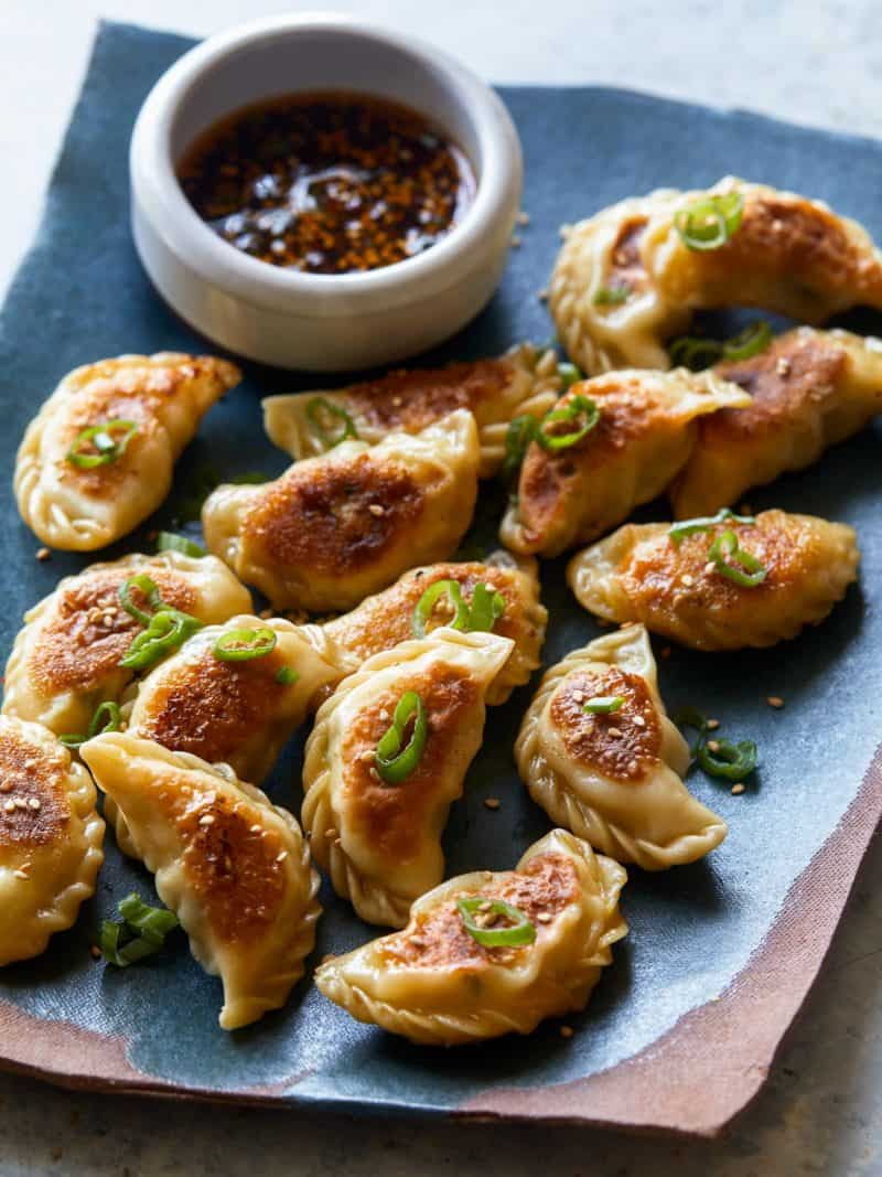 Crispy chicken pot stickers with green onions and sauce on a platter.