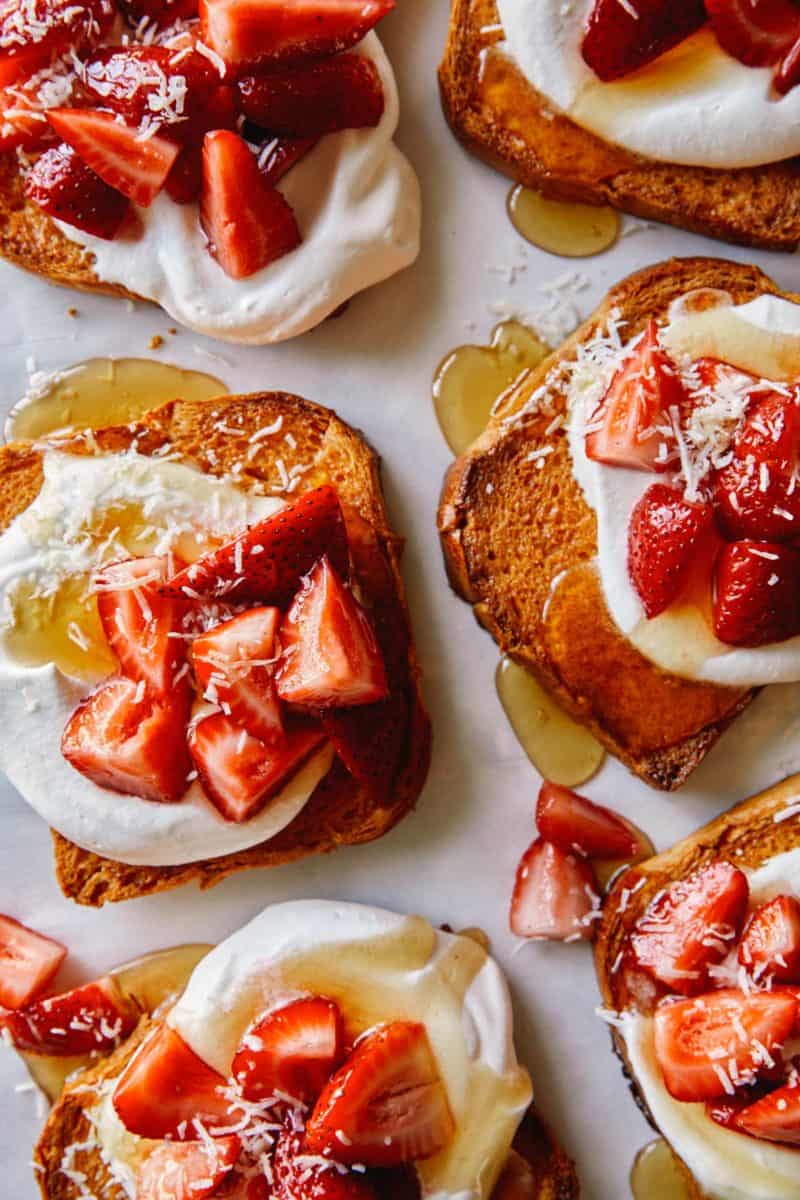 A close up of honey brick toast topped with whipped cream and strawberries.