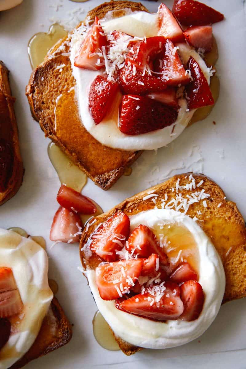 A close up of honey brick toast topped with whipped cream and strawberries.