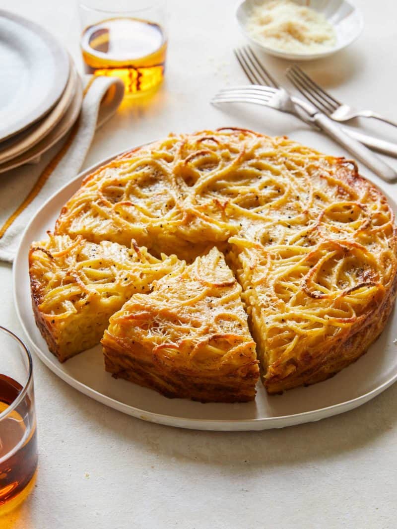 Cacio e pepe pasta pie with slices cut with plates and forks.