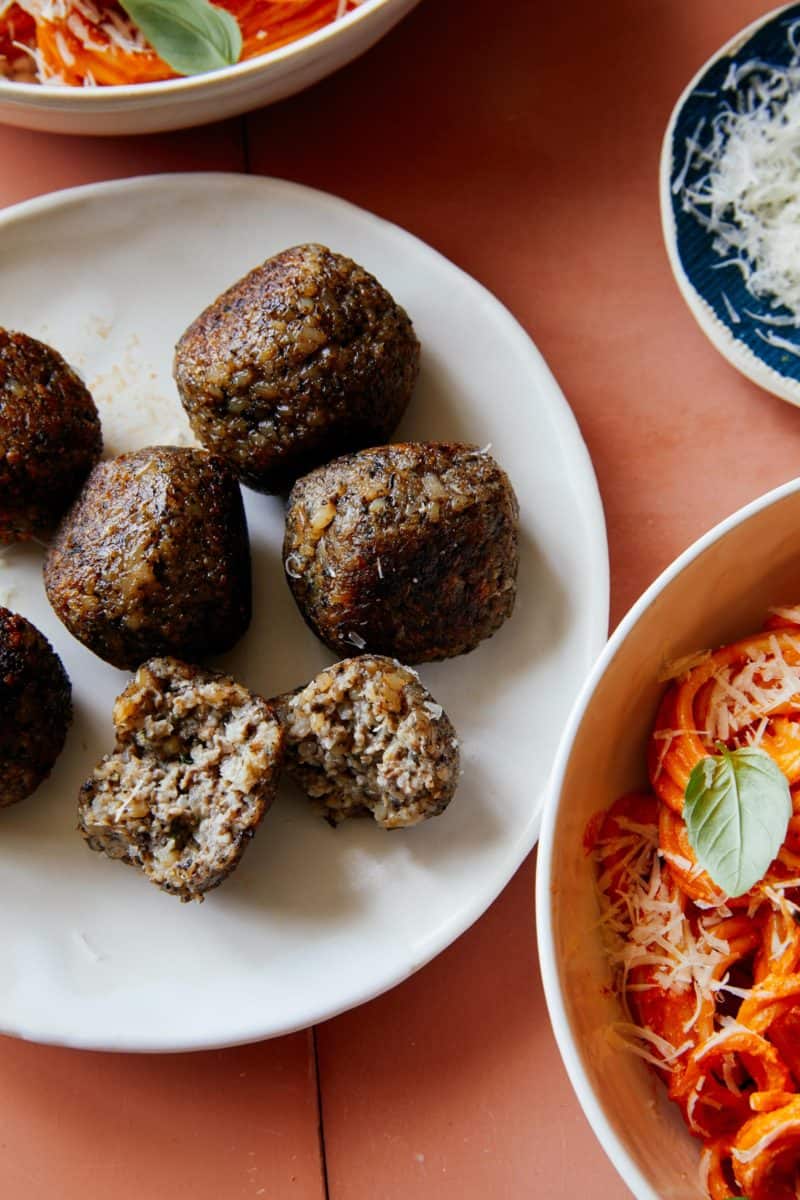 Vegan meatballs on a plate next to creamy roasted red pepper spaghetti.