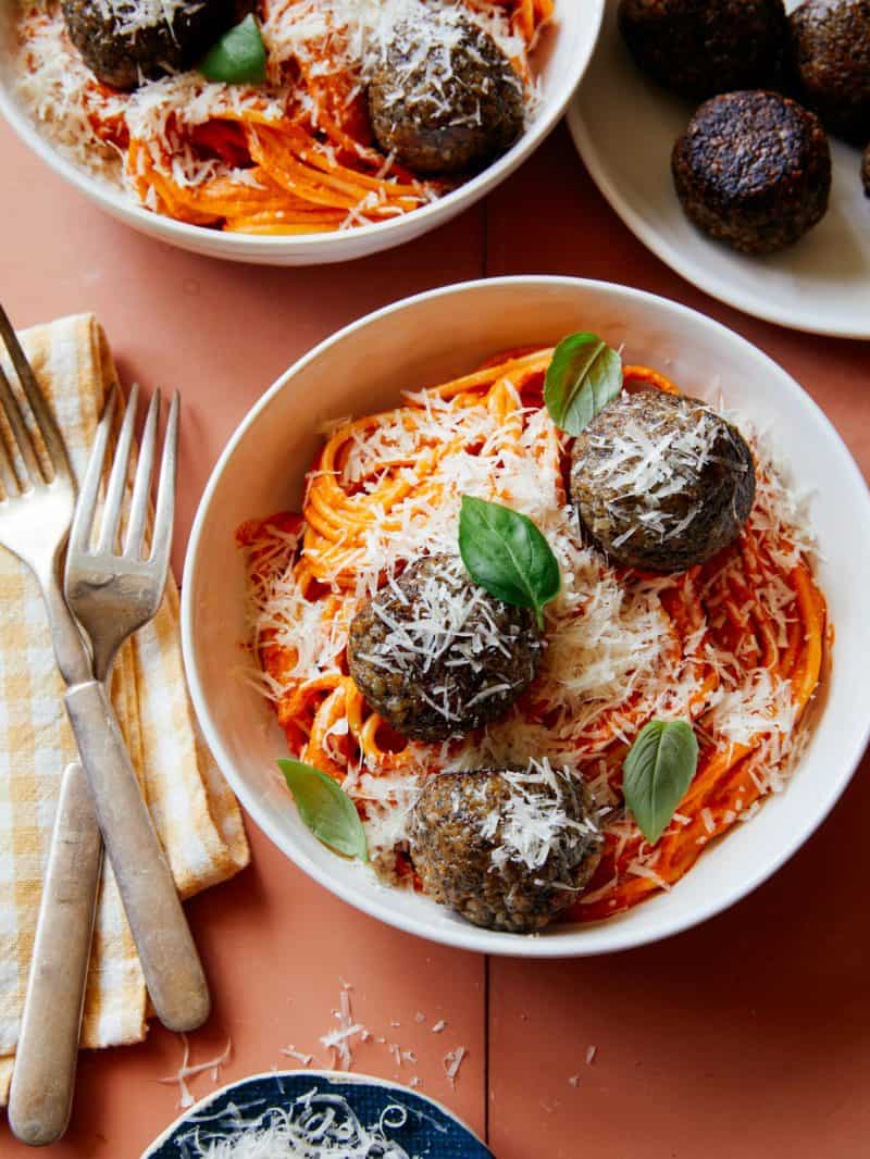 Vegan creamy roasted red pepper spaghetti and meatballs in a bowl with forks.