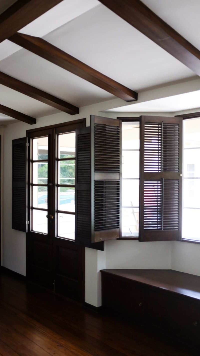 A room with large windows with open shutters and french doors.