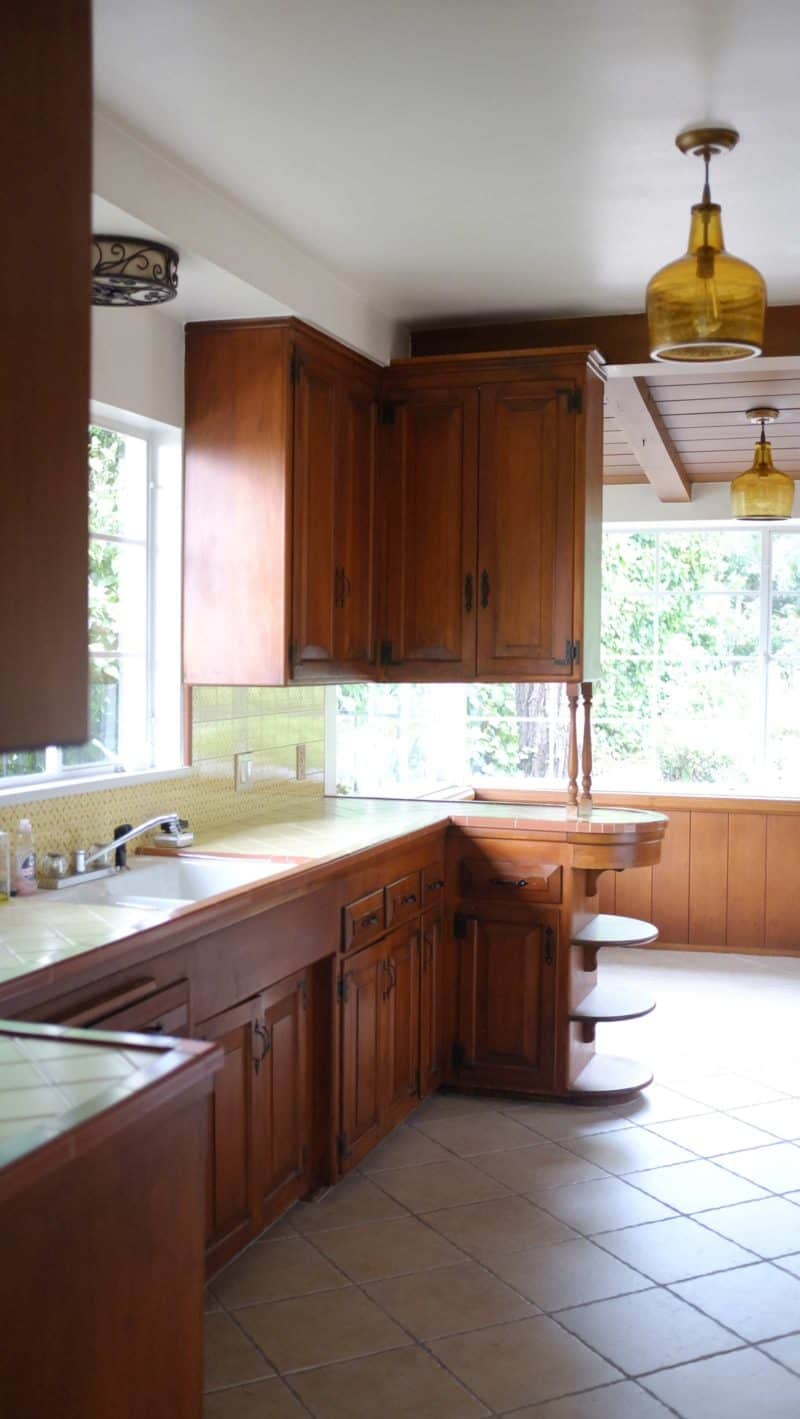 A kitchen with a sink and a window looking into eat in area.