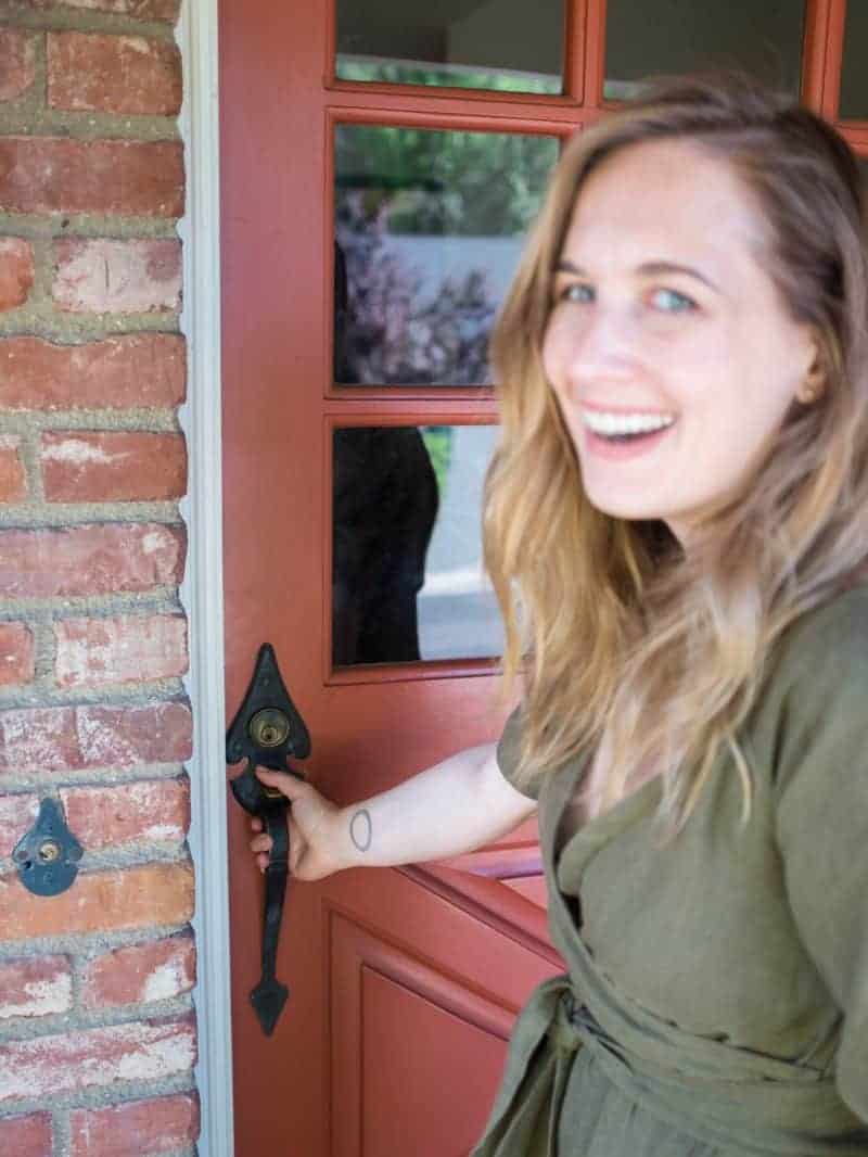 A beautiful blue eyed woman smiling while holding a door handle.