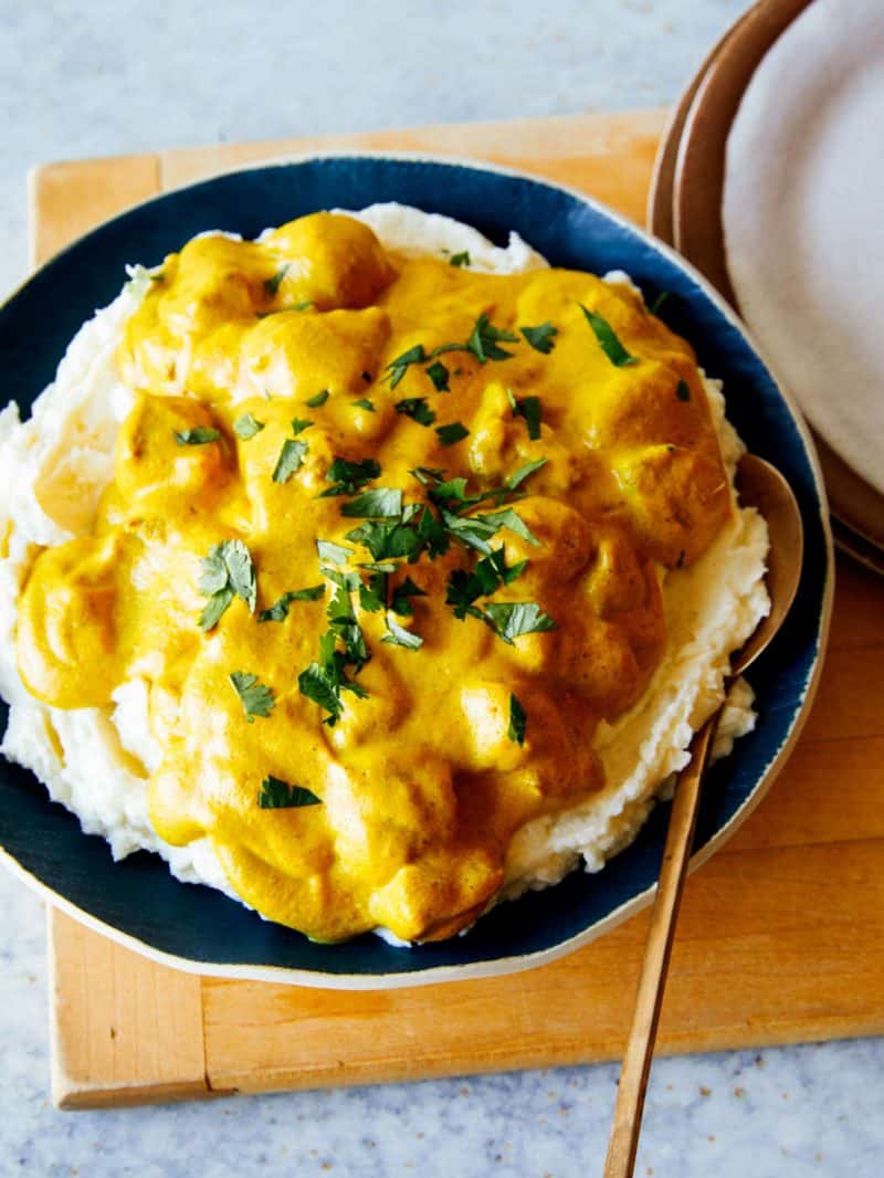 Chicken korma over mashed potatoes with a spoon.
