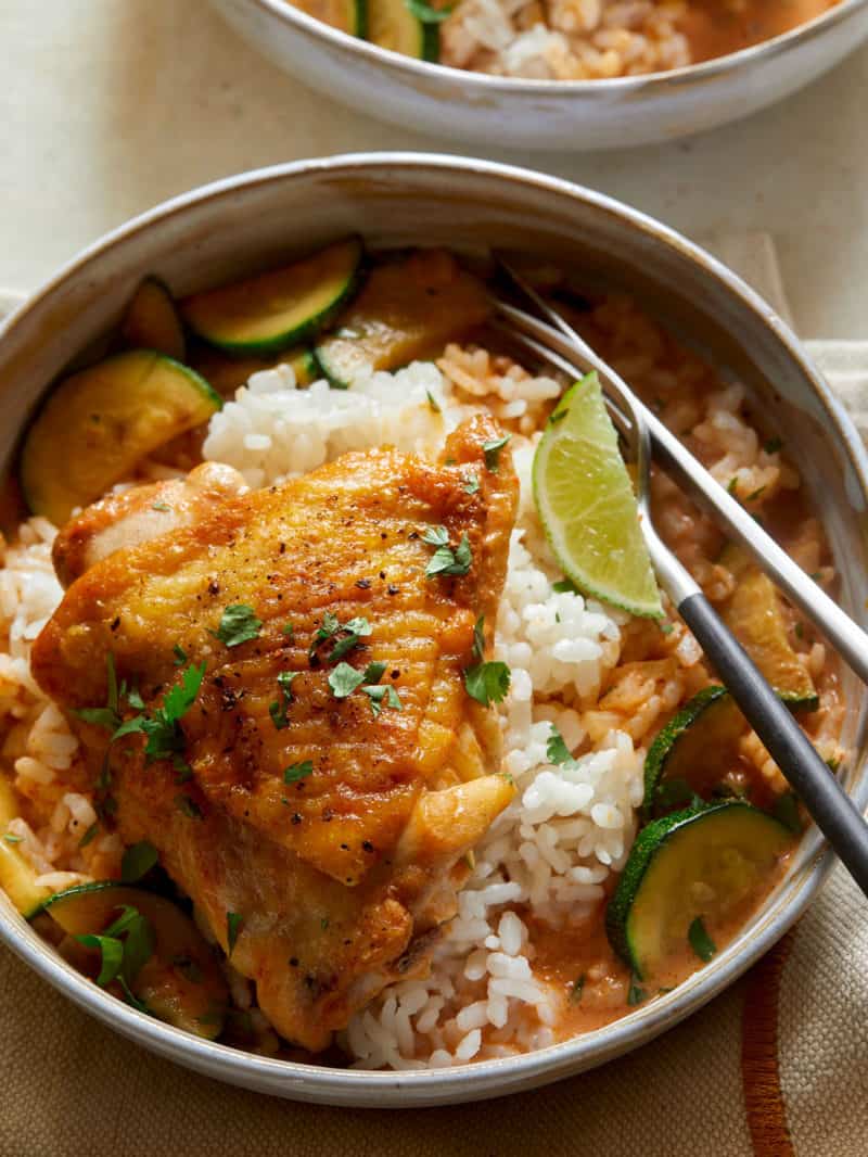 A close up of Thai red curry chicken thighs over white rice with a fork.