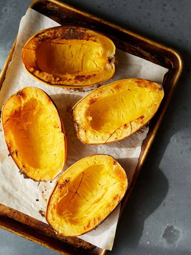 A sheet pan of several baked spaghetti squash halves.