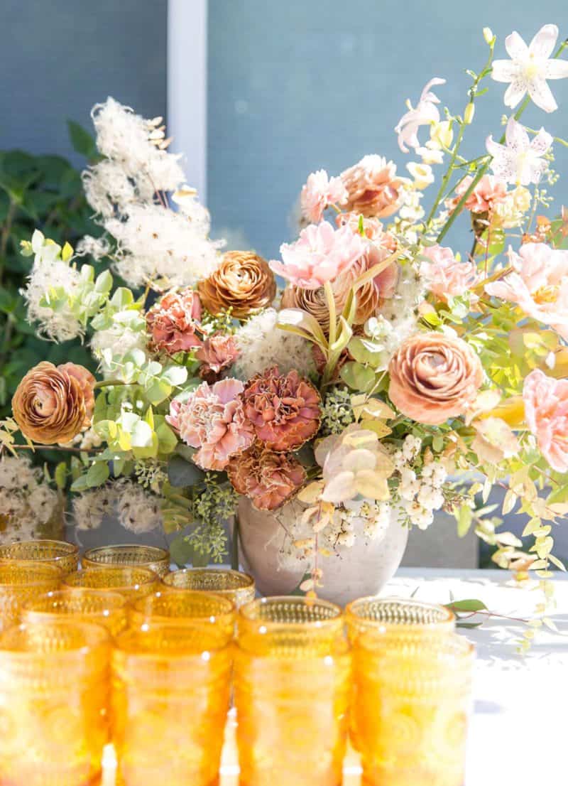 A large floral arrangement with drink glasses in front.