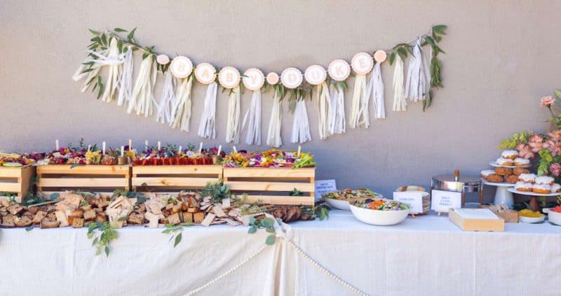 Table with charcuterie and cheese boards, salads, and a garland backdrop.