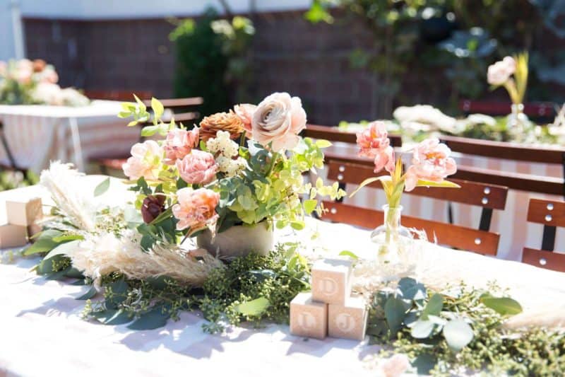 A floral arrangement with greenery and decorative blocks on a table.