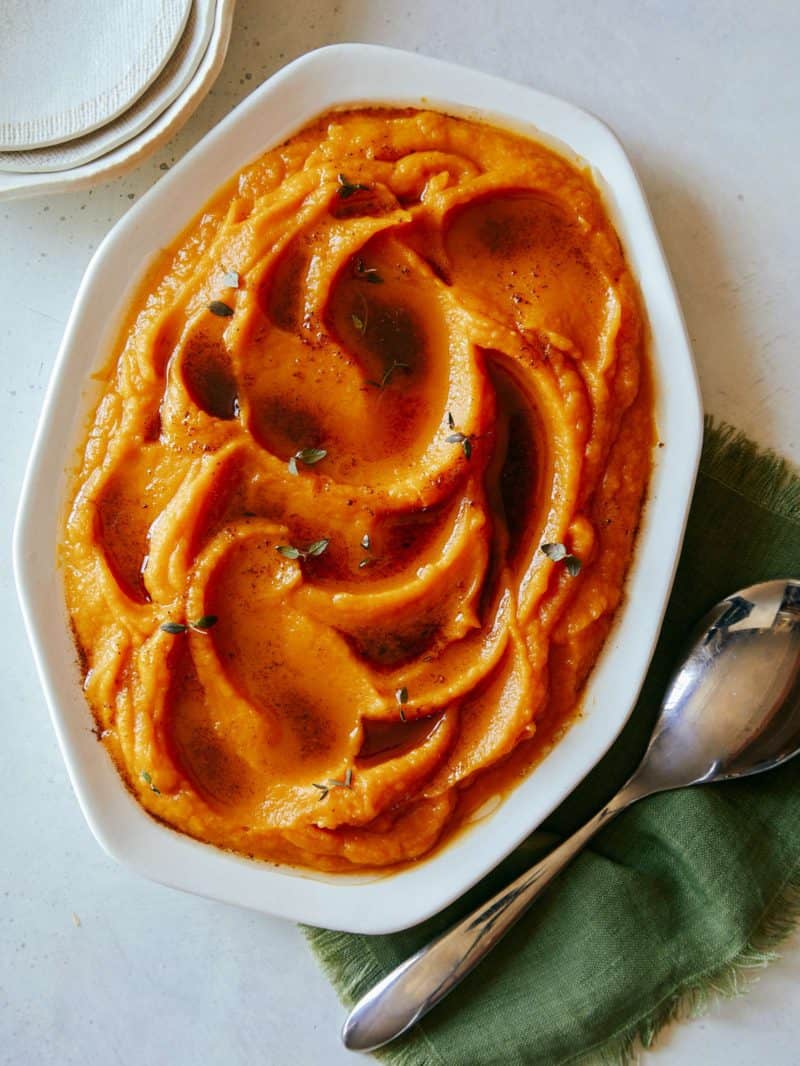 A large oval dish of butternut squash puree with browned butter and a spoon.