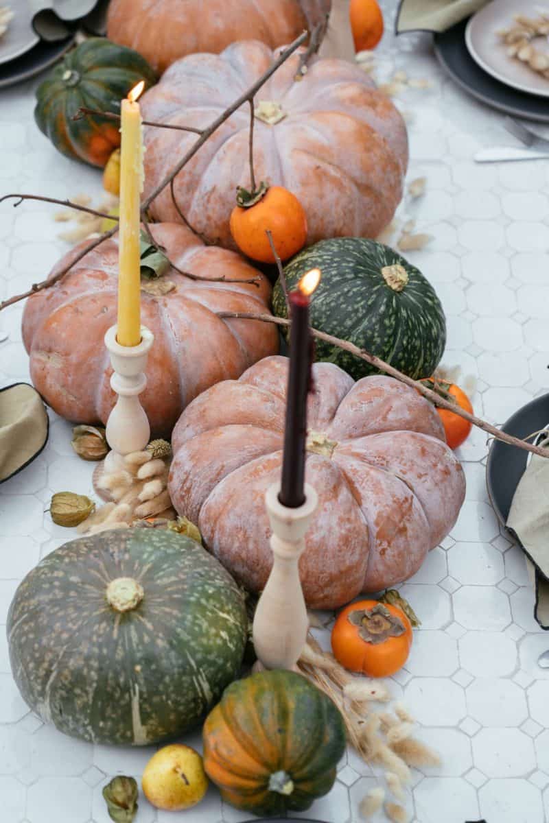 A close up of winter squash, fruits, dried bunny tails, and candles.