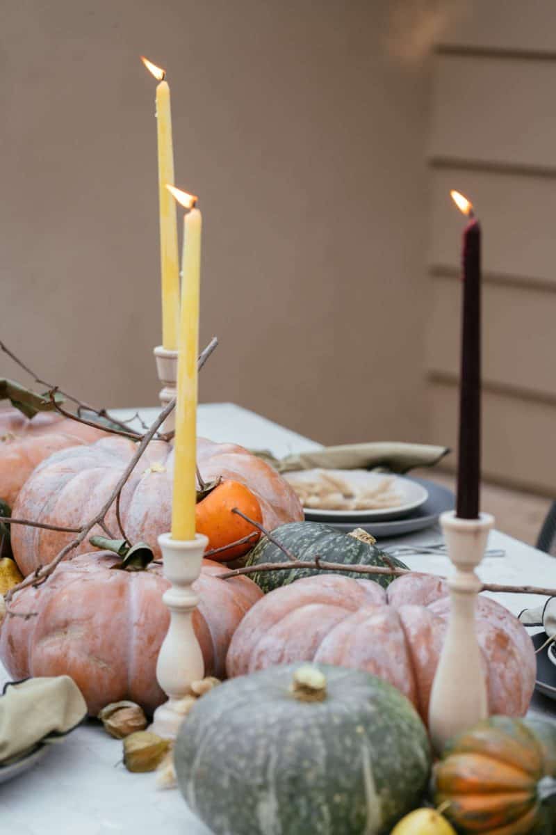 A close up of place settings, winter squash, fruits, and candles.