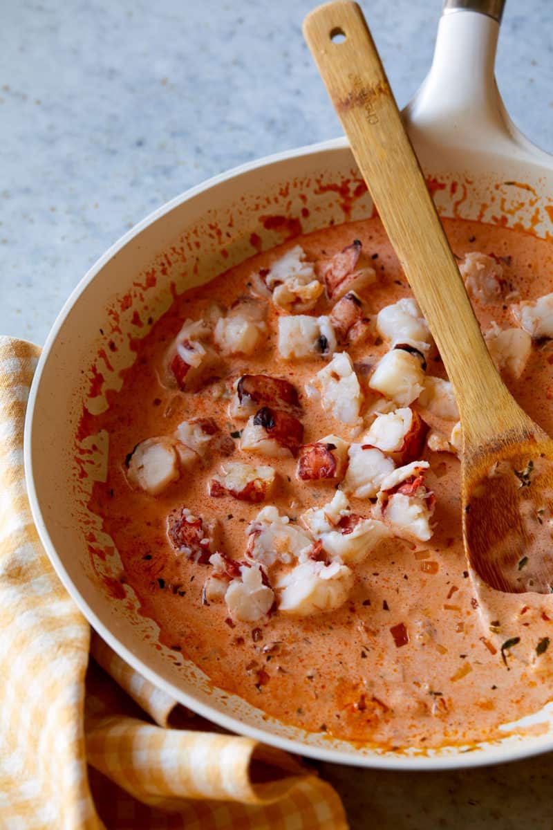 Creamy lobster pasta sauce in a bowl with a wooden spoon.