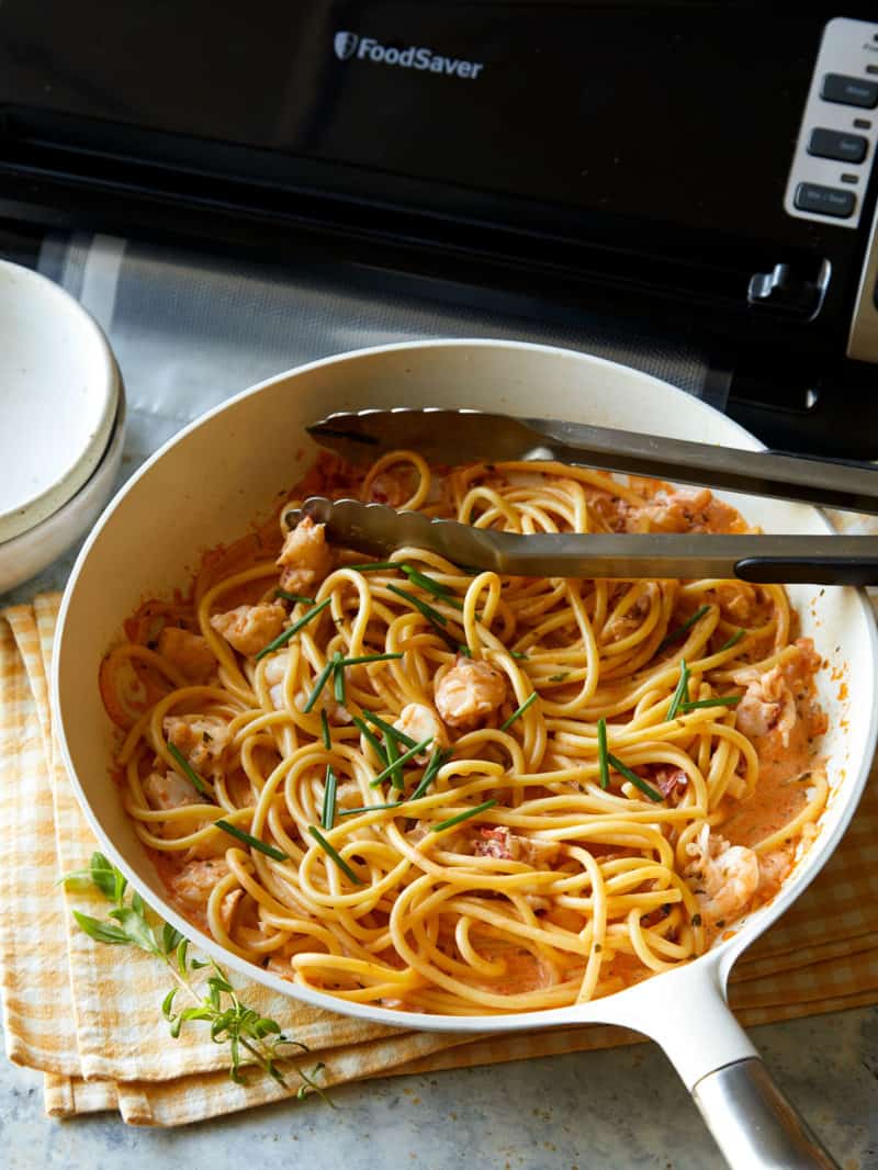 Creamy lobster pasta in a bowl with a metal tongs and food saver.