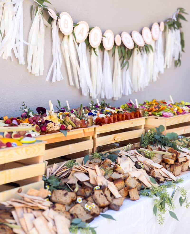 A close up of table with charcuterie and cheese boards, salads, and a garland backdrop.