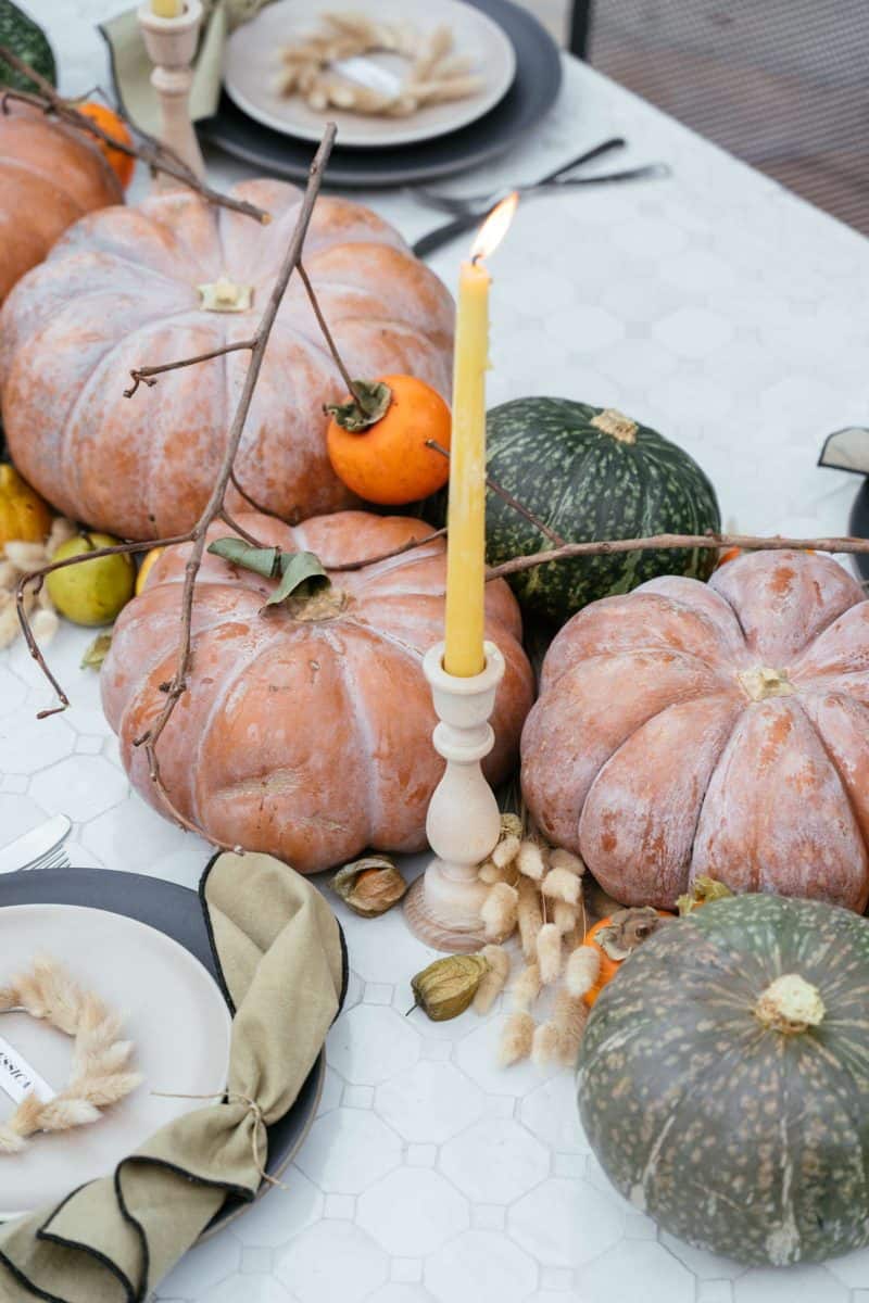 A close up of winter squash, fruits, dried bunny tails, and candles.