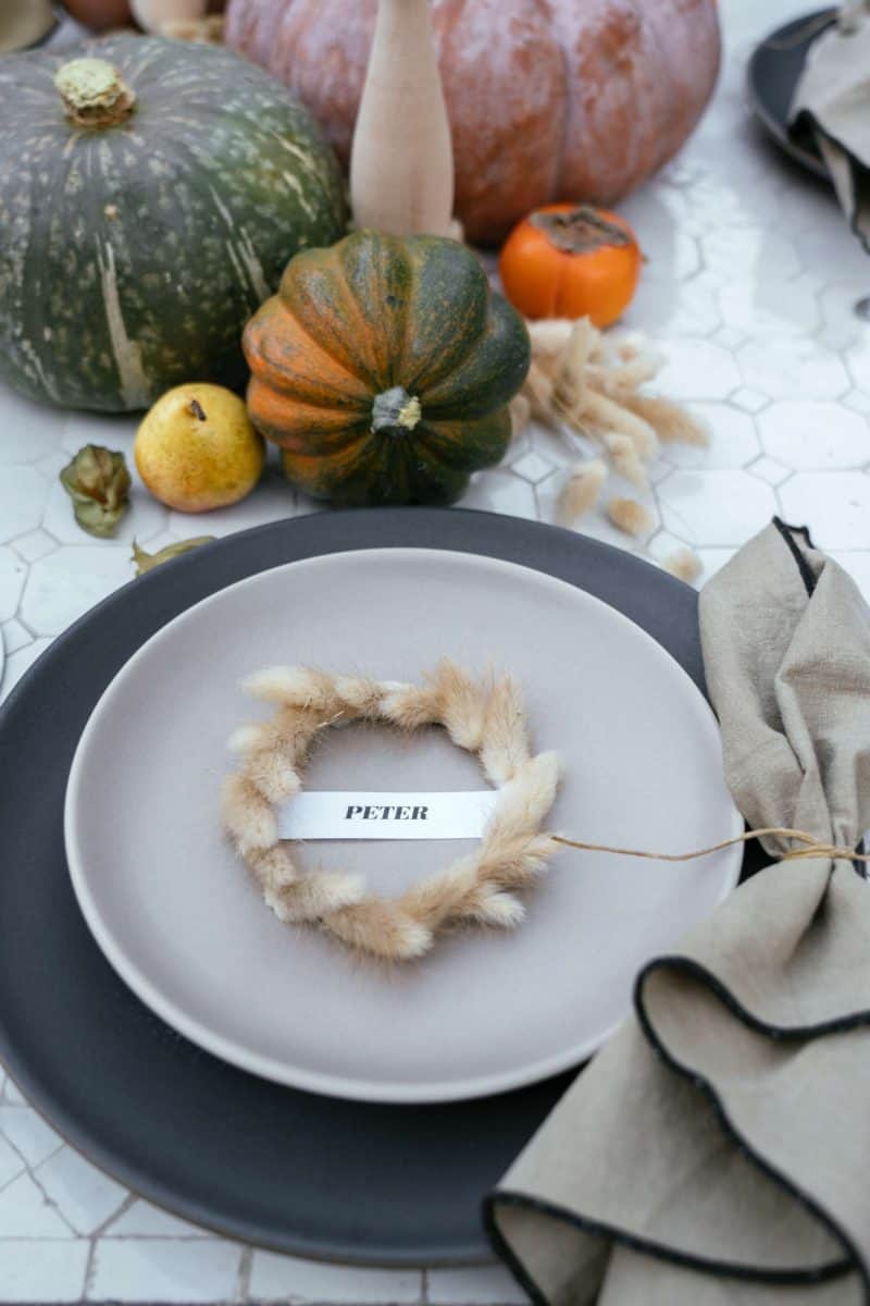 A place setting with a plate, mini wreath place card, and a napkin with table decor.