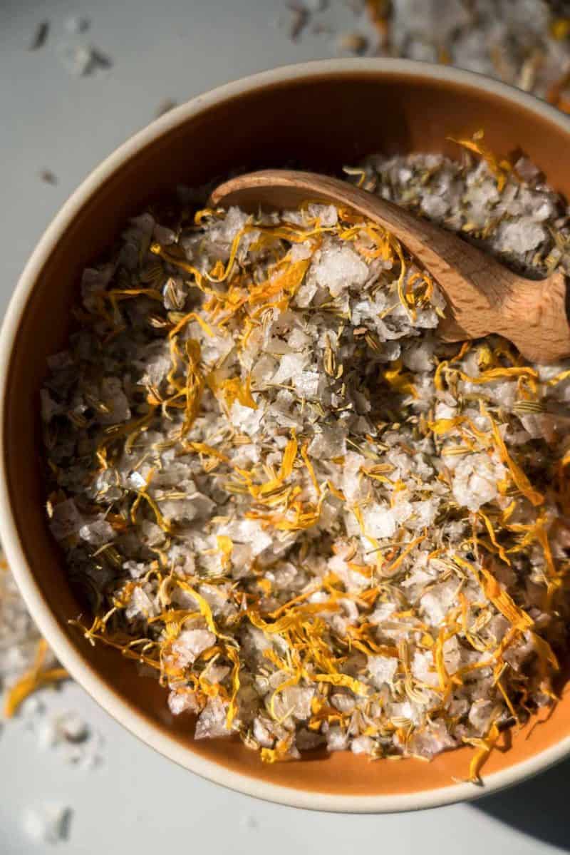 A close up of calendula, fennel and thyme salt in a bowl with wooden spoon.