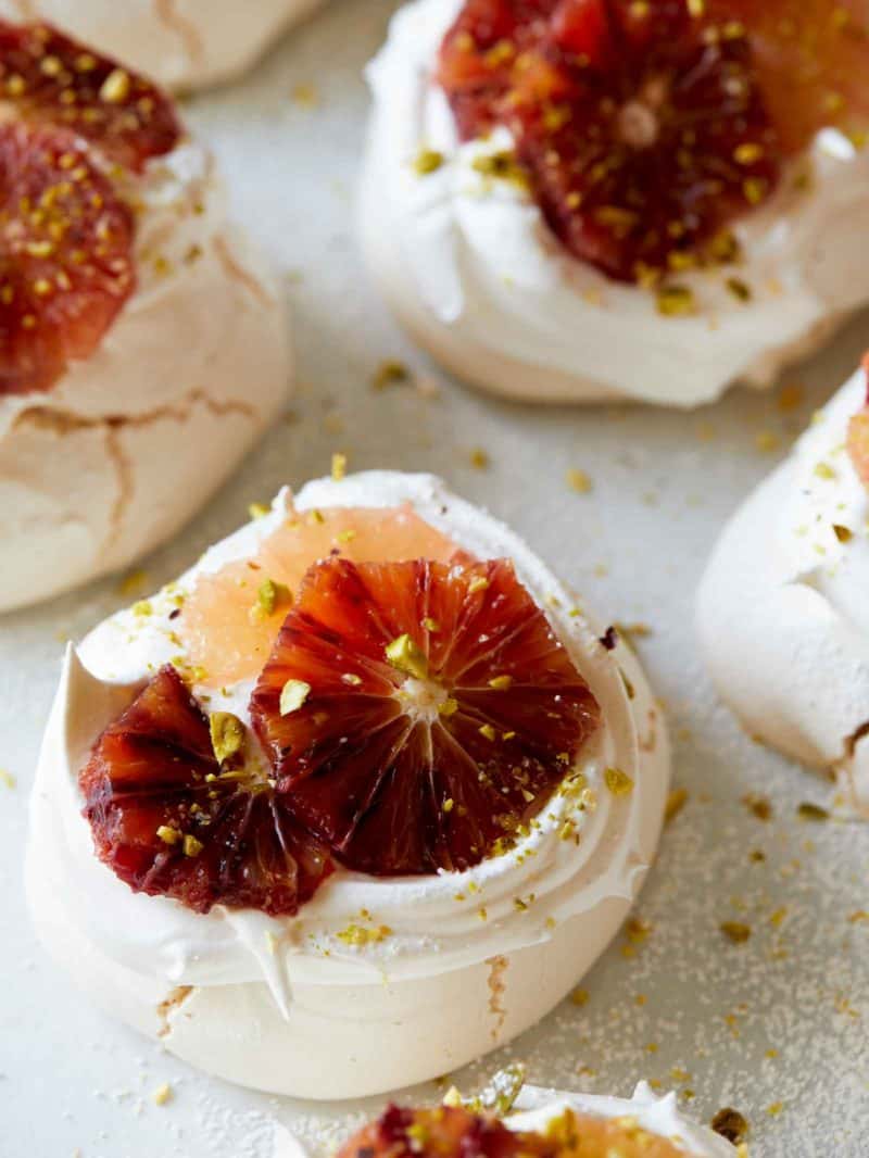 A close up of mini pavlovas with citrus on top.