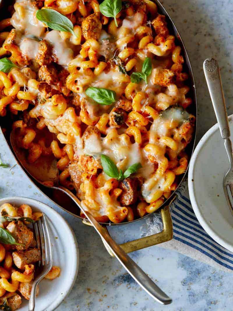 A pan of creamy pork baked pasta with serving spoon and plates with forks.