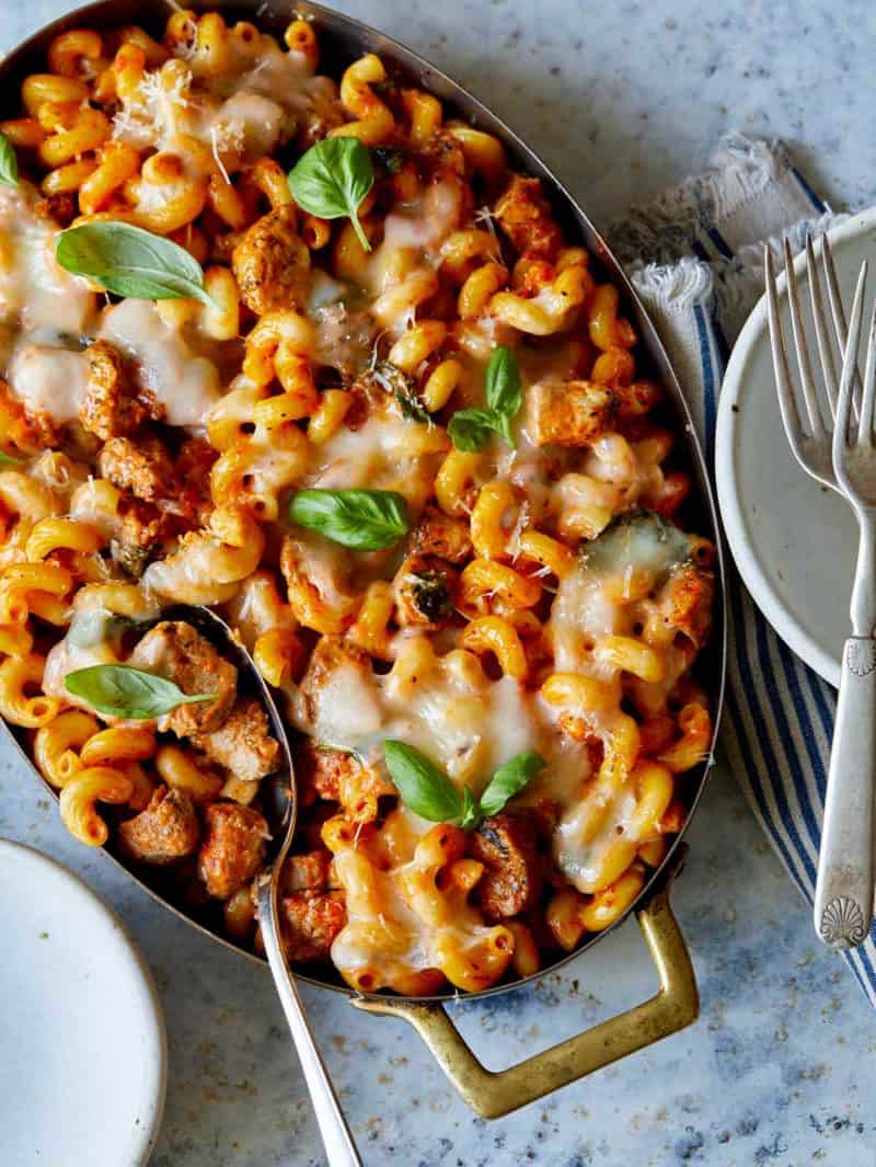A pan of creamy pork baked pasta with serving spoon and plates with forks.