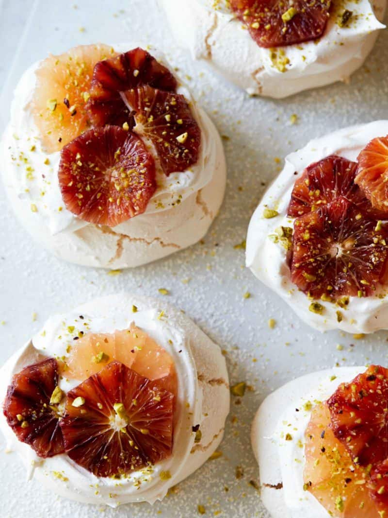 A close up of mini pavlovas with citrus on top.