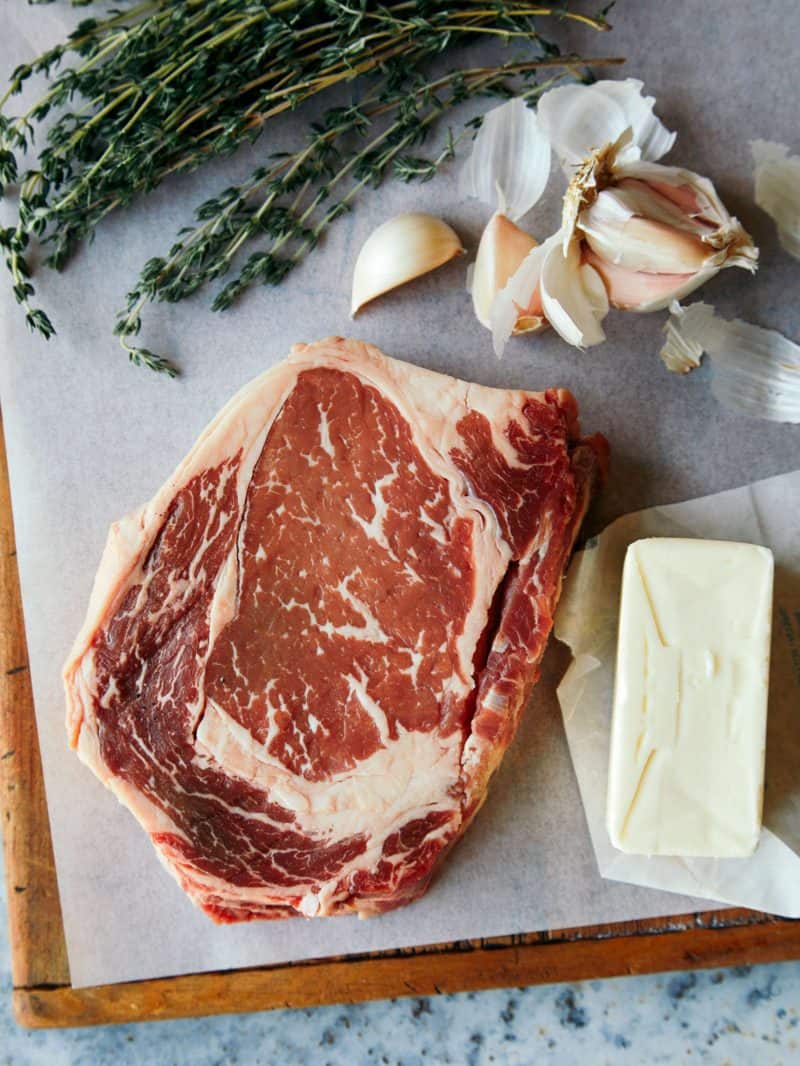 A piece of raw ribeye with herbs, garlic, and butter.