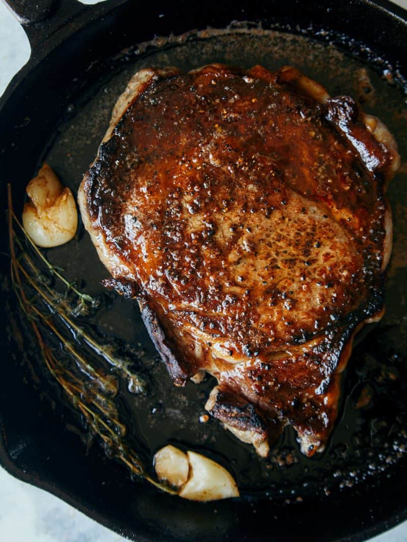 A close up of seared ribeye in a pan.