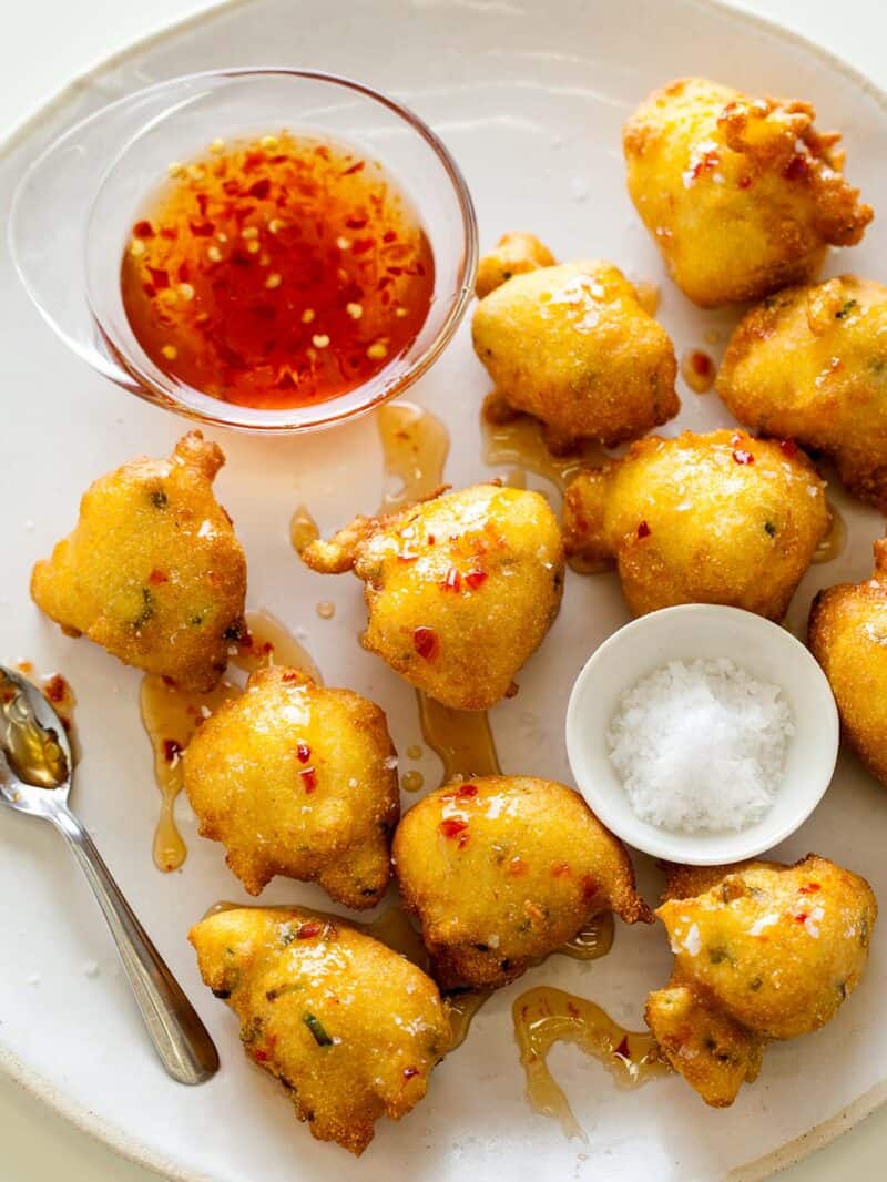 Hush puppies with small glass bowl of sauce, small white bowl of salt, and a spoon.