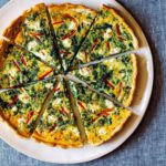 A close up on a spinach quiche with red bell peppers.