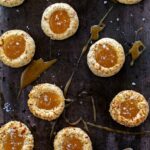 Salted caramel thumbprint cookies on a dark surface with caramel drizzled around.