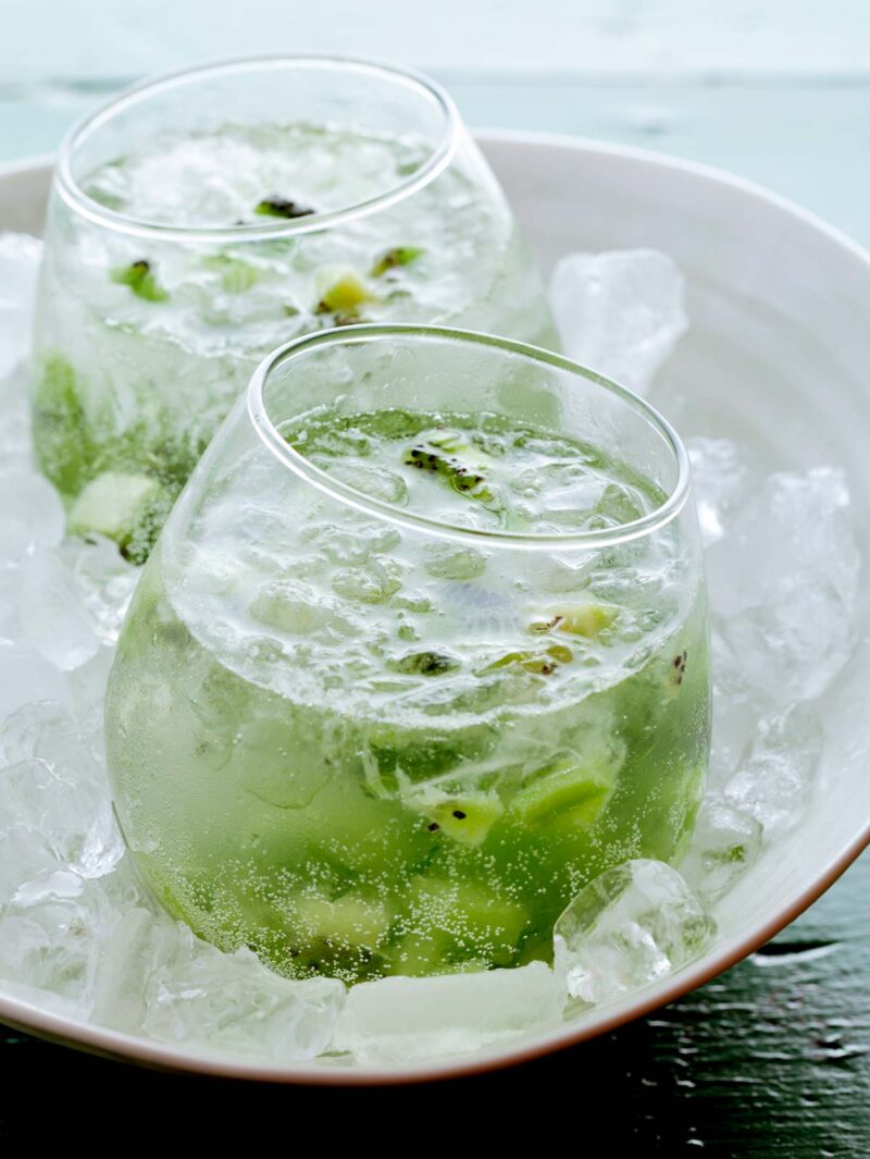 A close up of kiwi caipiroskas resting in a bowl of ice.