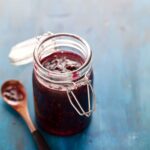 A close up of an open glass jar of simple blackberry jam with a wooden spoon.