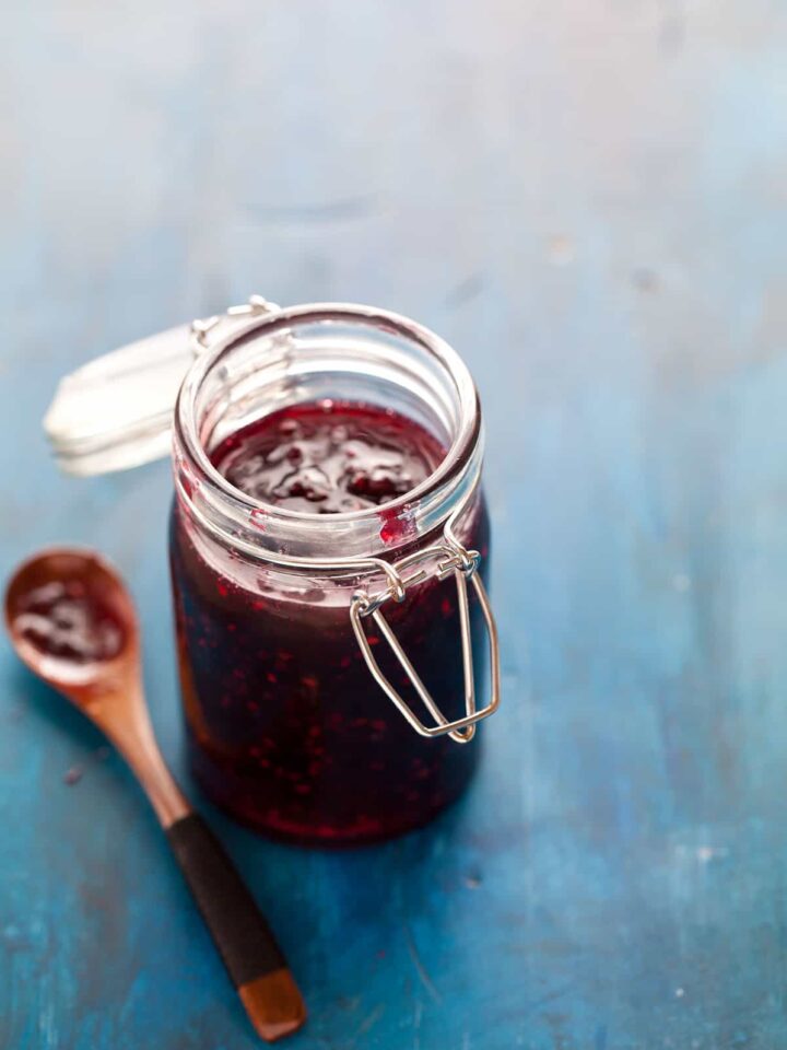 A close up of an open glass jar of simple blackberry jam with a wooden spoon.