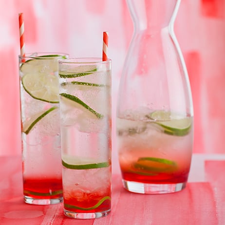 Sweet cherry gin and tonics with lime wheels and straws next to a half full carafe.