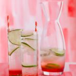 Sweet cherry gin and tonics with lime wheels and straws next to a half full carafe.