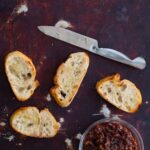 Crostini with a knife and a bowl of boozy bacon jam.