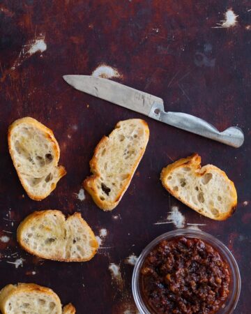 Crostini with a knife and a bowl of boozy bacon jam.