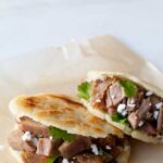 A close up of arepas filled with carnitas and guasacaca.