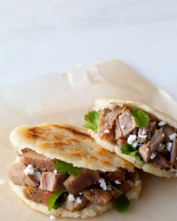A close up of arepas filled with carnitas and guasacaca.