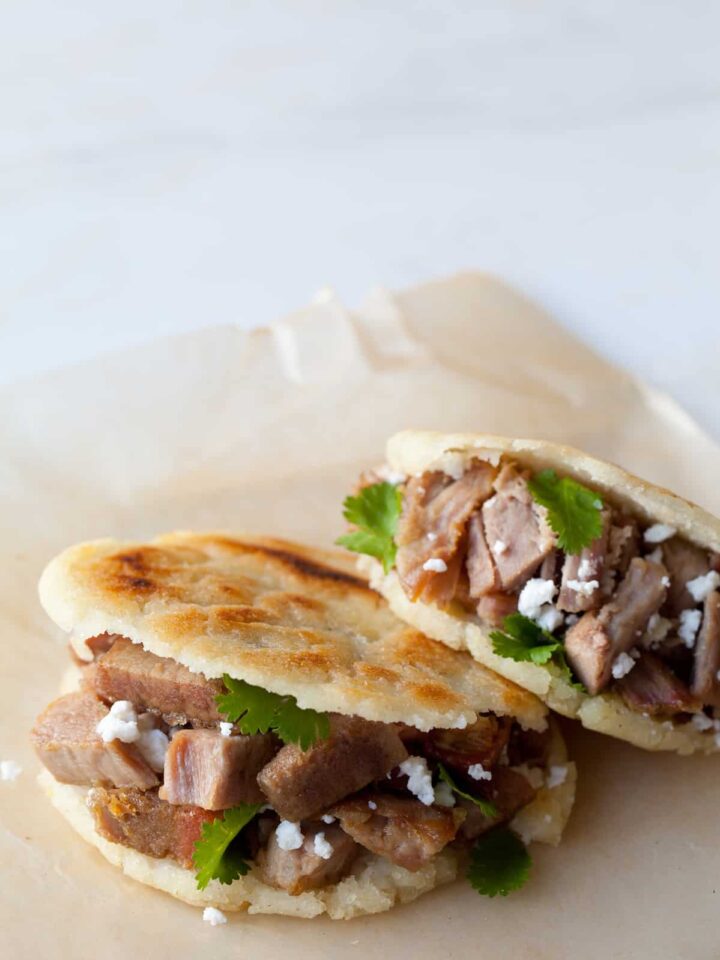 A close up of arepas filled with carnitas and guasacaca.