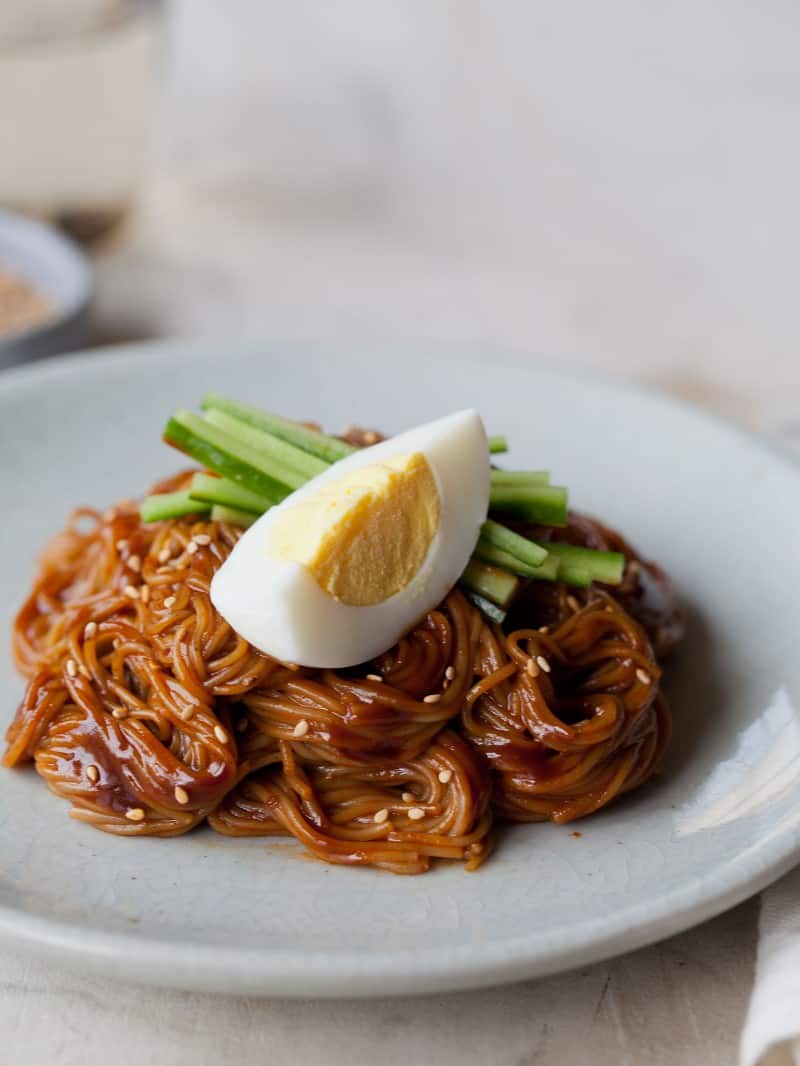 A close up of bibim nengmyun with a hard boiled egg wedge and cucumber garnish.